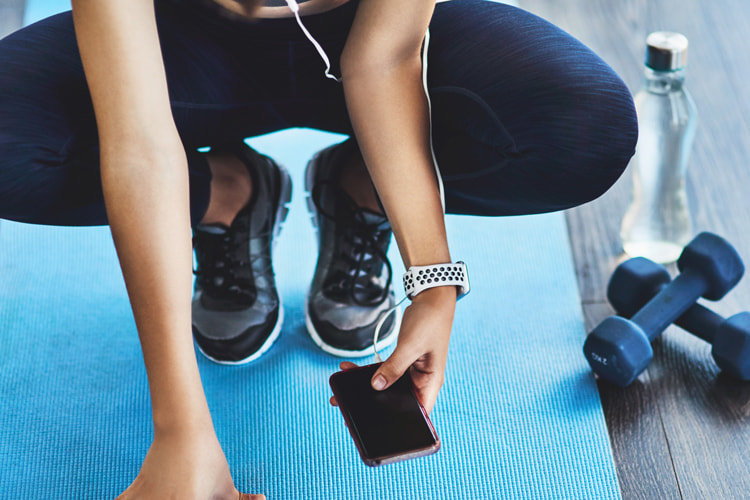 woman in workout clothing squatting on gym mat looking at smart phone